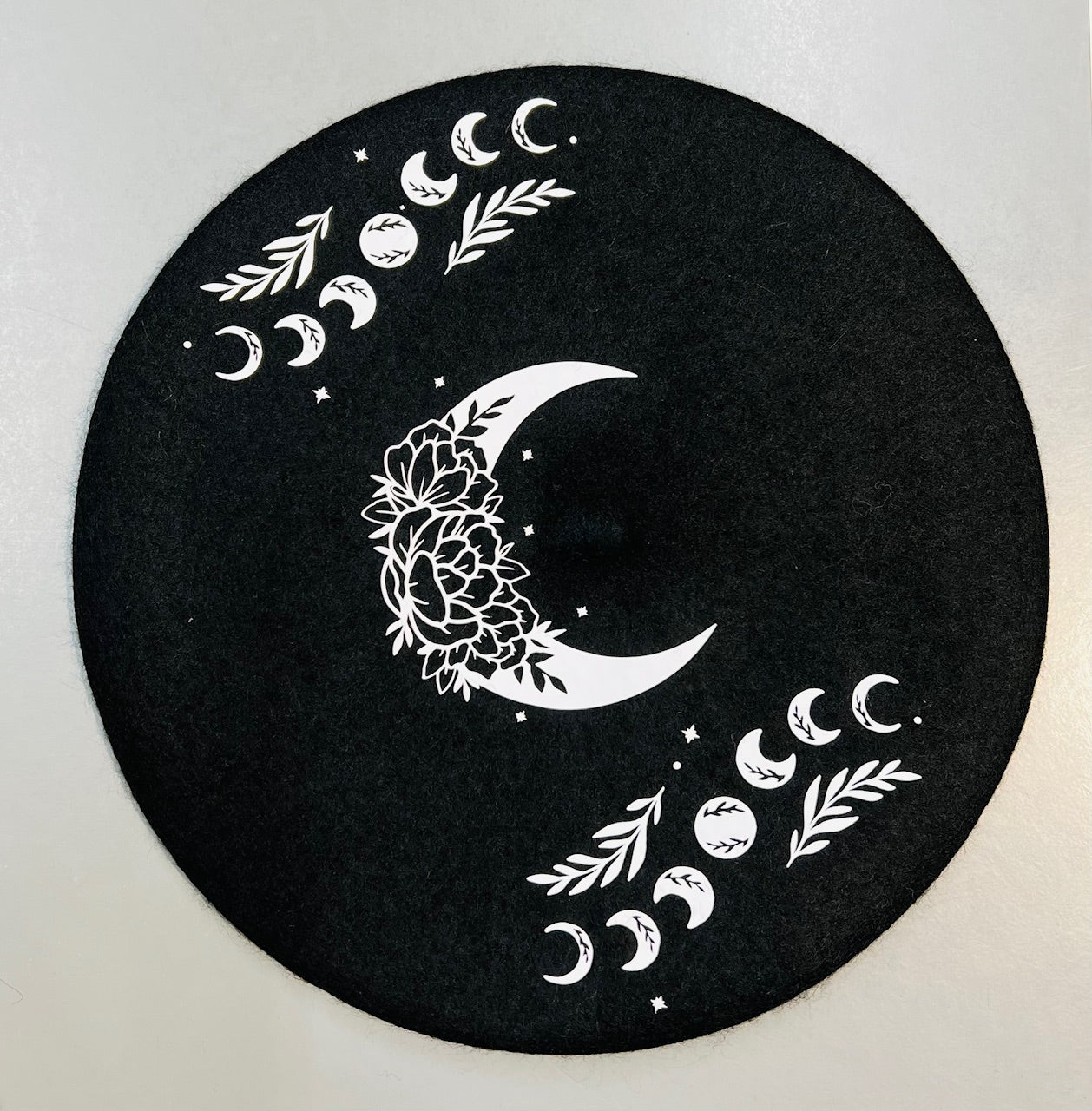 Black circular mat with white moon and leaf designs on a light gray background