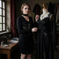 Woman in a black dress standing next to a mannequin in a room with sewing equipment.