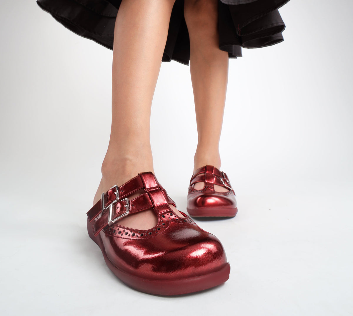 Red metallic shoes worn with a black skirt on a light gray background