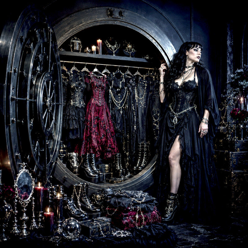 Woman in a dark, gothic-themed room with dresses and candles.